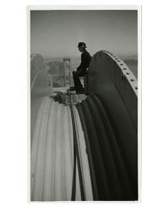 Bridge worker resting atop cable pulley, circa 1936